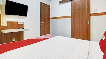 Ein Hotelzimmer mit einem Bett, einem an der Wand montierten Fernseher, einem Holzschrank und einem Regal mit einem Gemälde.