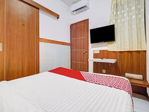 Habitación de hotel con cama, armario de madera, televisor y una pequeña estantería.