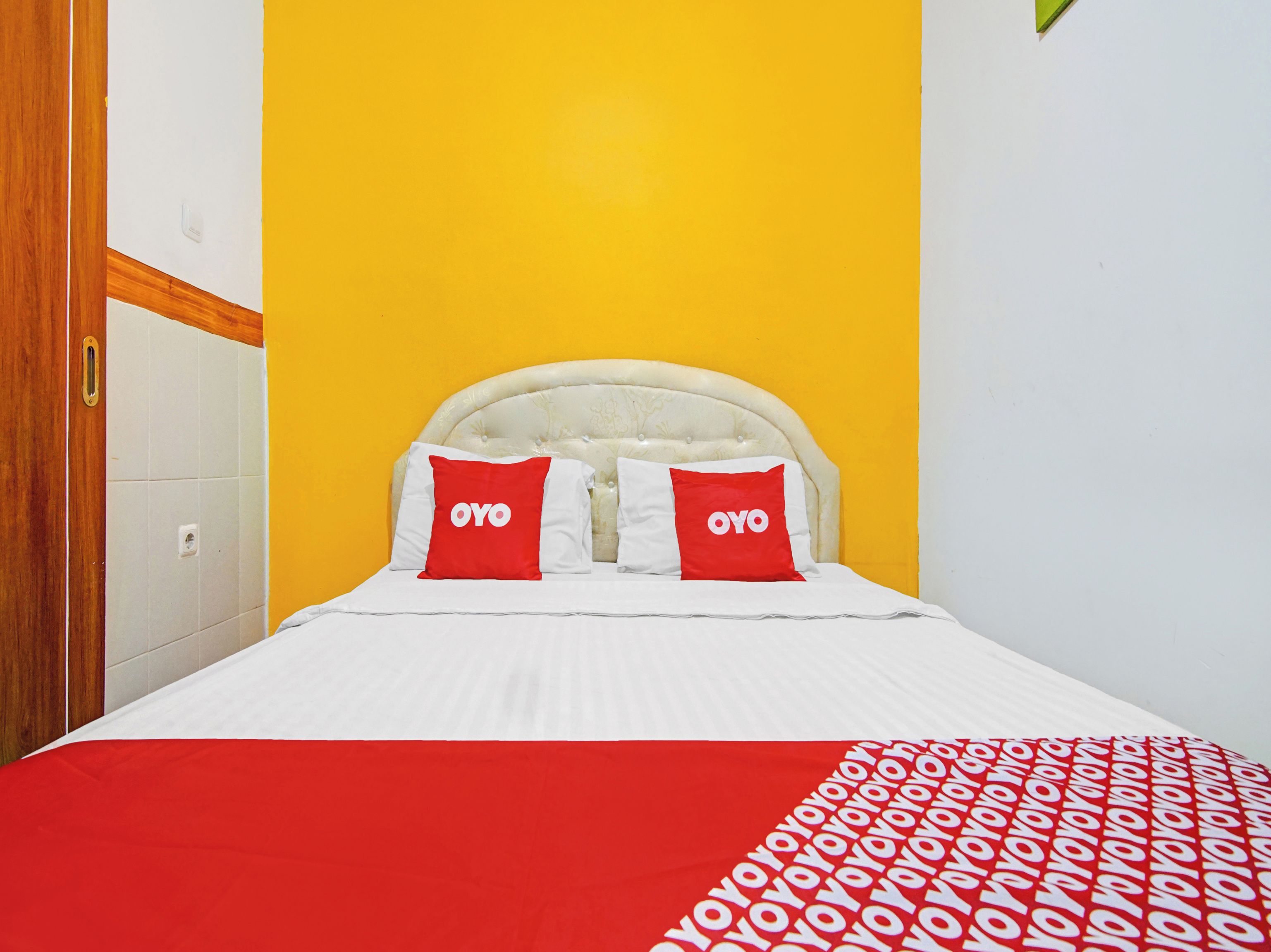 Una cama con cabecera blanca, dos almohadas con la marca 'OYO' y una colcha de cuadros rojos y blancos.