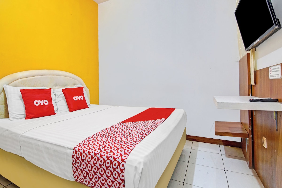 Una habitación de hotel con una cama, televisión y un escritorio de madera.