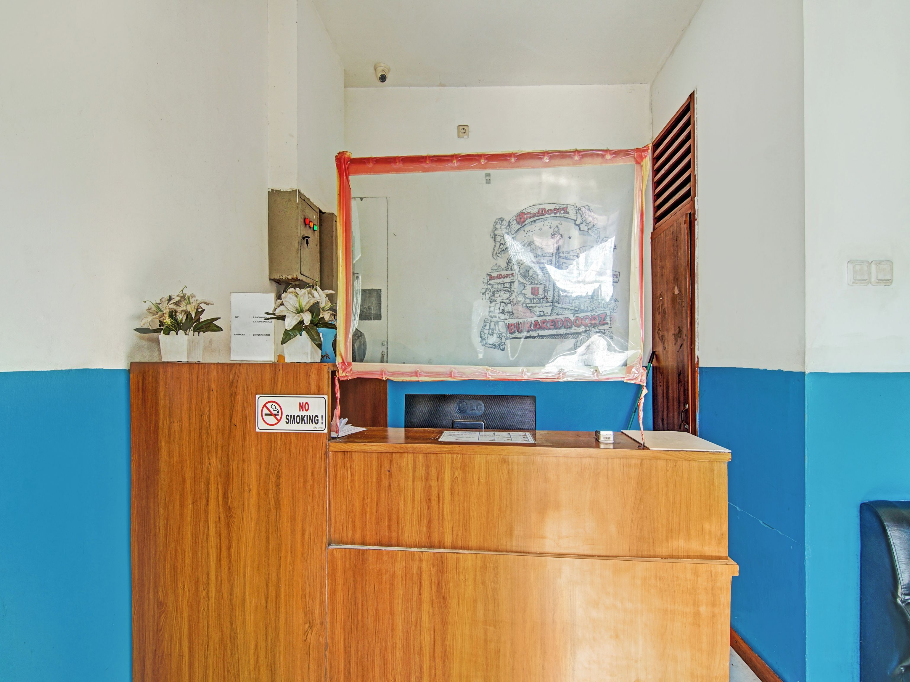 A reception desk with a 'No Smoking' sign, a wooden counter, a blue wall, and a window with a map.