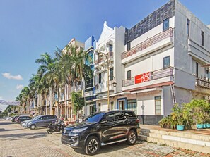 Een meerlaags gebouw met een commerciële begane grond, een parkeerplaats met auto's en een rij palmbomen.