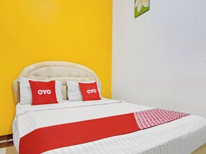Una cama con cabecera blanca, dos almohadas con la marca 'OYO' y una colcha con estampado rojo y blanco.