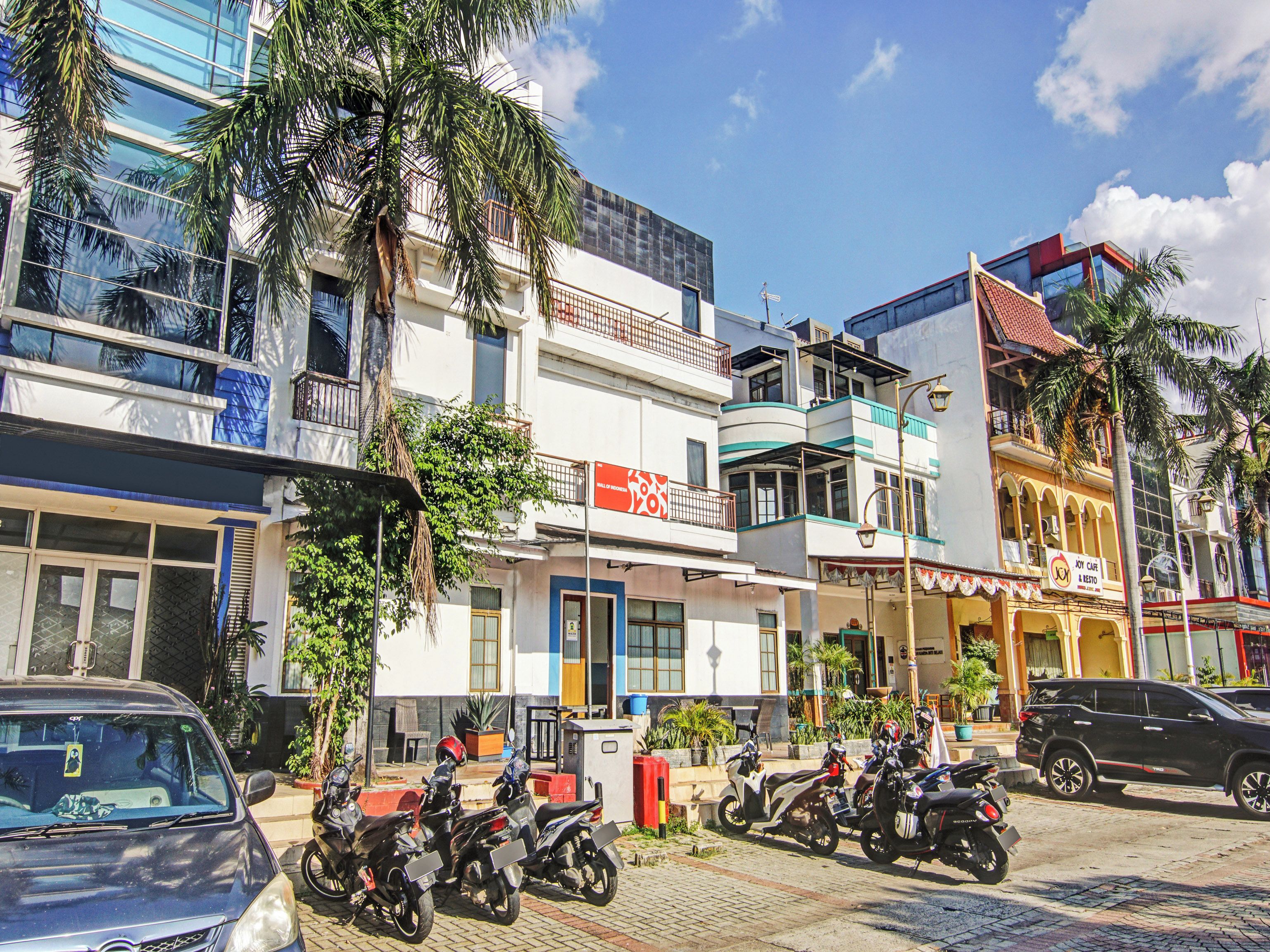 A street view with multiple buildings, parked motorcycles, and a car.