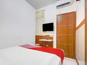 Un dormitorio con una cama, un televisor montado en la pared, una puerta de madera y un lavamanos pequeño y blanco.