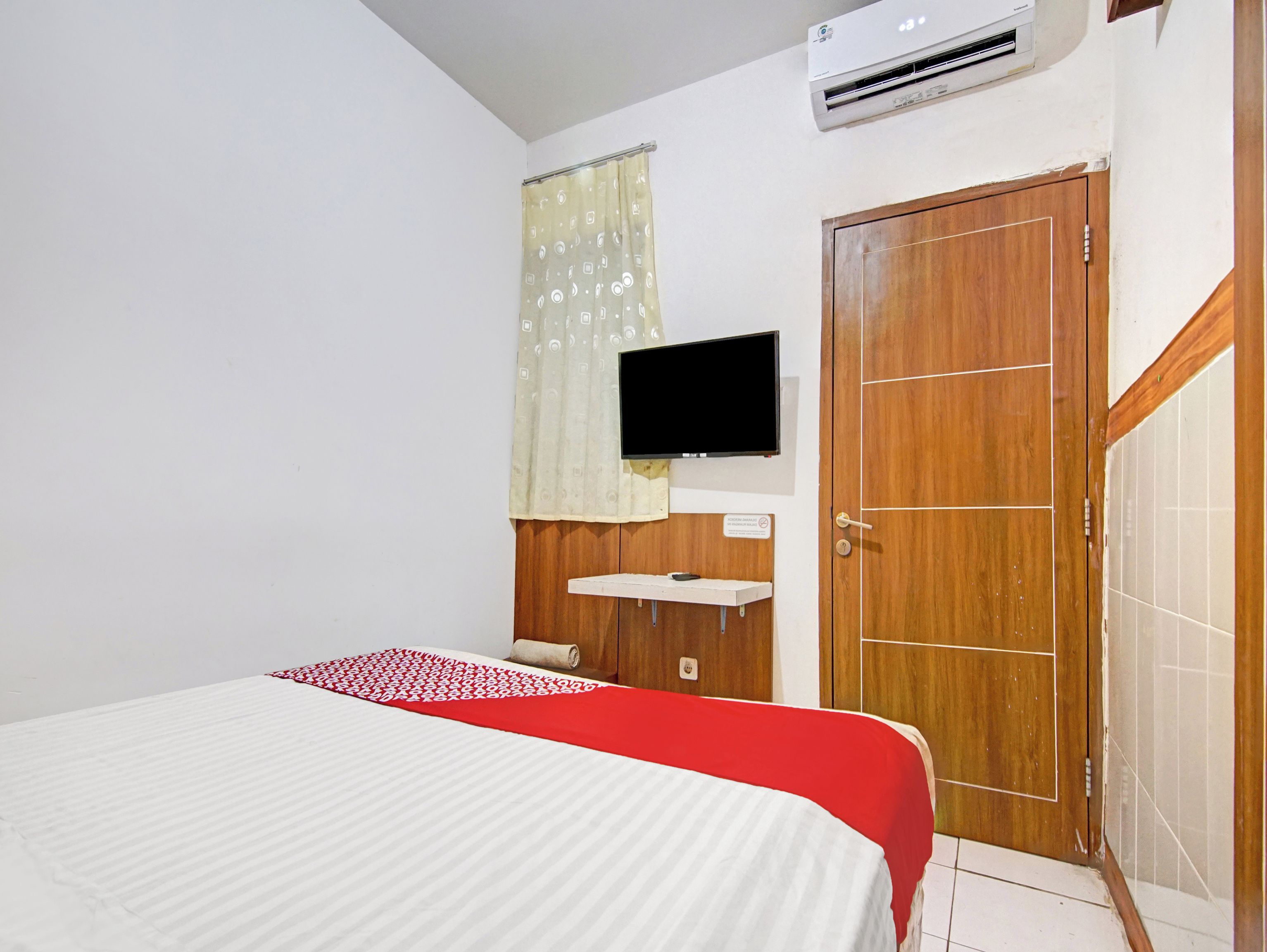 A bedroom with a bed, a TV mounted on the wall, a wooden door, and a small white sink.
