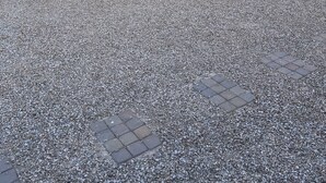 Un patio con mesa y sillas, suelo de grava y un edificio con ventanas y puerta.
