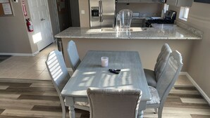 Un comedor con una mesa y sillas, una cocina al fondo y un extintor en la pared.