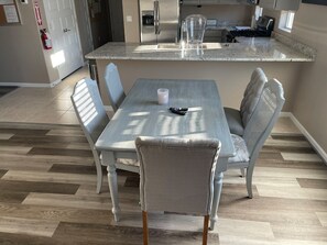 A dining area with a table and chairs, a kitchen in the background, and a fire extinguisher on the wall.