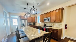 A modern kitchen with granite countertops, wooden cabinets, stainless steel appliances, and a central island with seating. - BEACHBLOCK FIRST HOUSE FROM BEACH WITH POOL OCEANVIEW 4 DECKS NEAR BOARDWALK (North Wildwood)