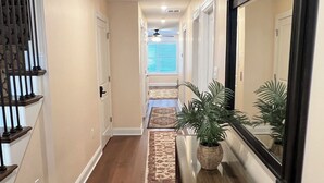 A hallway with a wooden staircase, a mirror, and a console table with a plant. - BEACHBLOCK FIRST HOUSE FROM BEACH WITH POOL OCEANVIEW 4 DECKS NEAR BOARDWALK (North Wildwood)