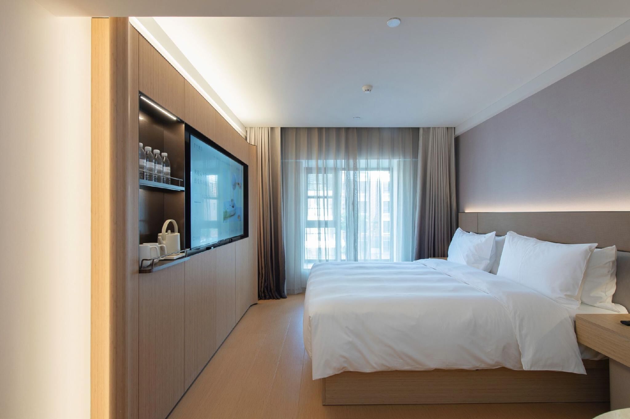 Habitación de hotel con una cama, un televisor montado en un mueble de madera, una ventana con cortinas y una mesita de noche.