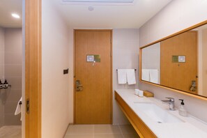 A hotel bathroom with a wooden door, a large mirror, a white sink, and a shower area. - Ji Hotel (Xiamen)
