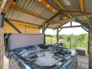 Un jacuzzi bajo una pérgola de madera con vistas a la vegetación.