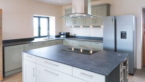 A modern kitchen with a central island, stainless steel appliances, and a window providing natural light. - Bowland Barn (Lancaster)