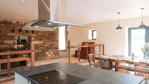 A modern kitchen with a stone wall, a built-in stove, and a dining area with wooden furniture. - Bowland Barn (Lancaster)