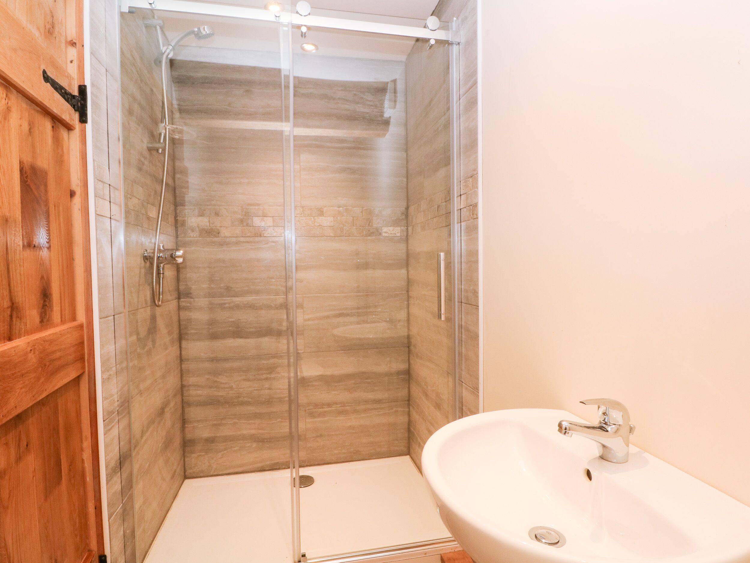A bathroom with a glass-enclosed shower, a wooden door, and a white sink.