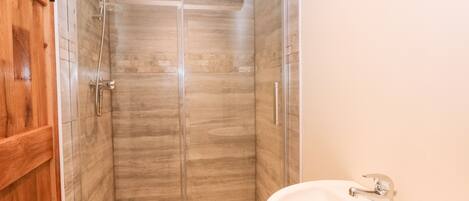A bathroom with a glass-enclosed shower, a wooden door, and a white sink.