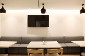 Et moderne interiør med en lang, grå sofa, to hvide borde og træstole. Et fladskærms-tv er monteret på væggen over sofaen.