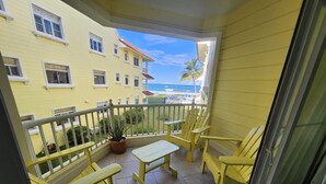 Een balkon met gele stoelen en een tafel, met uitzicht op een strand en een geel gebouw.