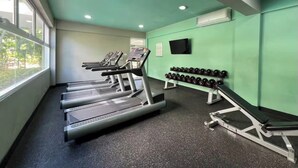 Een fitnessruimte met loopbanden, gewichten en een televisie aan de muur.