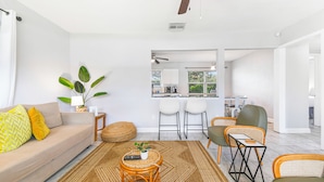 A modern living room with a sofa, chairs, a coffee table, and a kitchen in the background. - Cozy 2 BR Home, walking distance to Crystal Beach/Park - Quaint Family Getaway! (Palm Harbor)