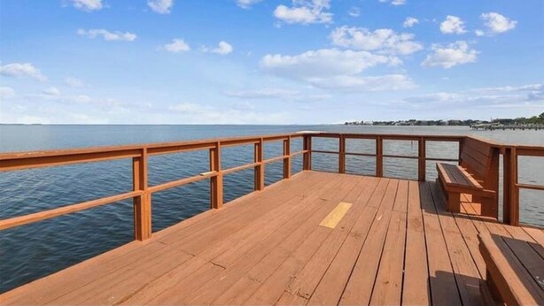 A wooden deck with a railing overlooking a calm body of water and a clear sky. - Cozy 2 BR Home, walking distance to Crystal Beach/Park - Quaint Family Getaway! (Palm Harbor)