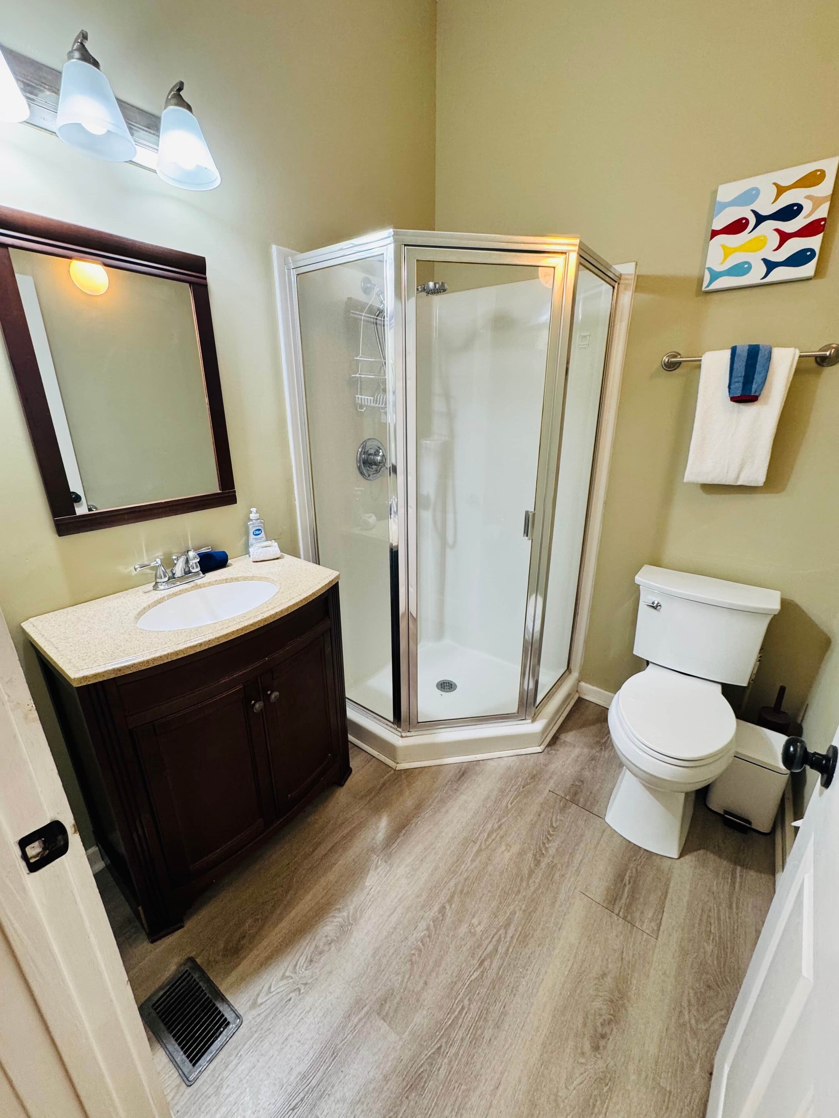 Un baño con cabina de ducha de vidrio, lavamanos con espejo y un inodoro.