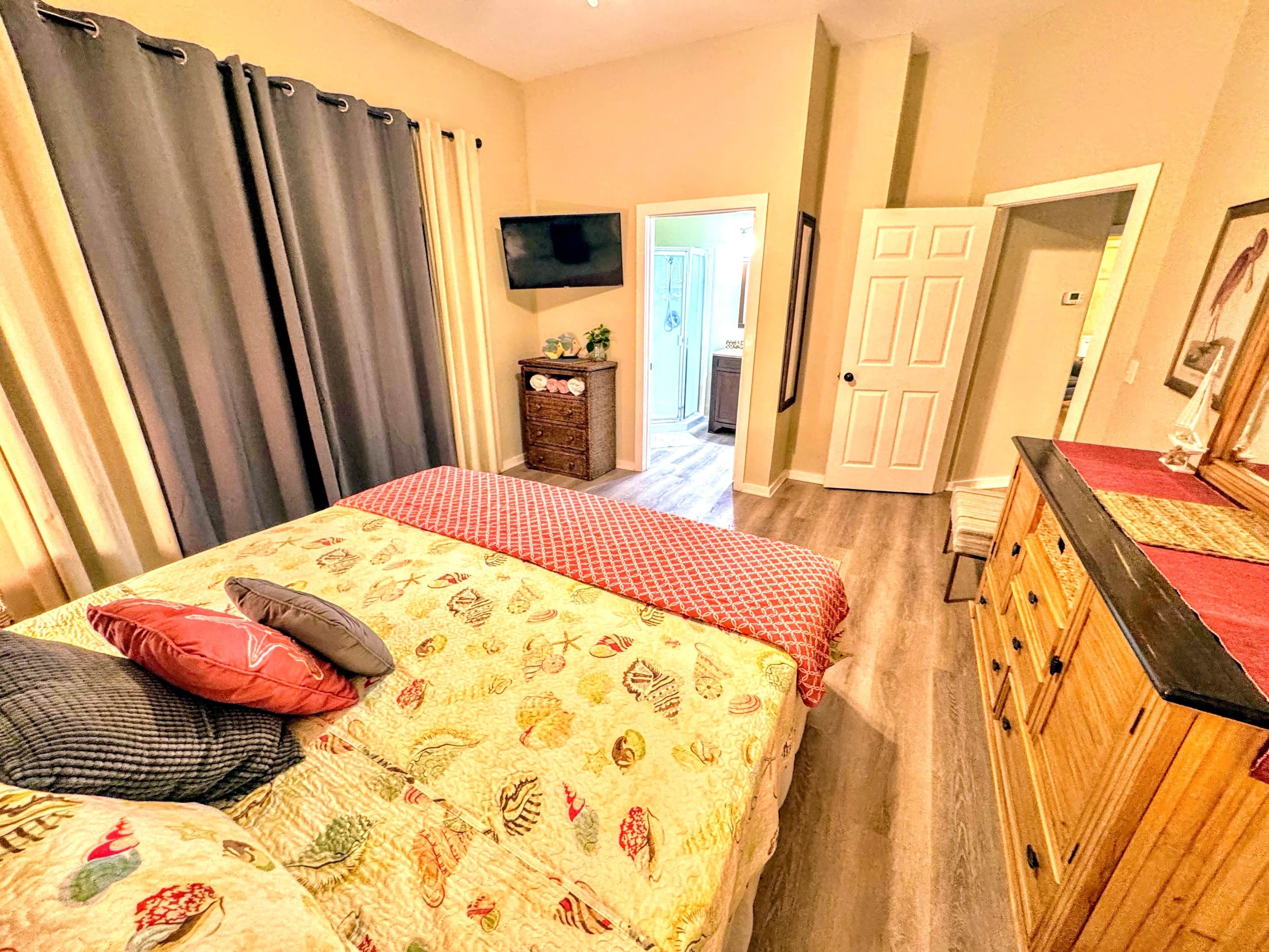 Une chambre à coucher comprenant un lit, une commode, un téléviseur et une porte donnant sur une autre pièce.