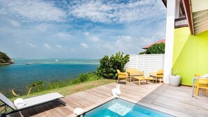 Una terraza de madera con piscina, sillas amarillas y vista al mar.