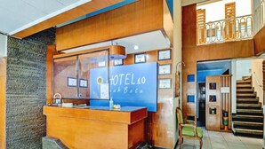 Un hall d'accueil d'hôtel avec un comptoir de réception en bois, des certificats encadrés et un escalier menant à un étage supérieur.