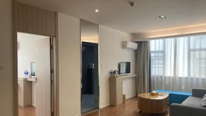Habitación de hotel moderna con piso de madera, una mesa redonda para café, un sofá, un televisor y una puerta corredera que da a un baño.