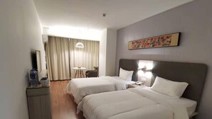 Habitación de hotel con dos camas, un escritorio, una silla, una mesa y un cuadro en la pared.