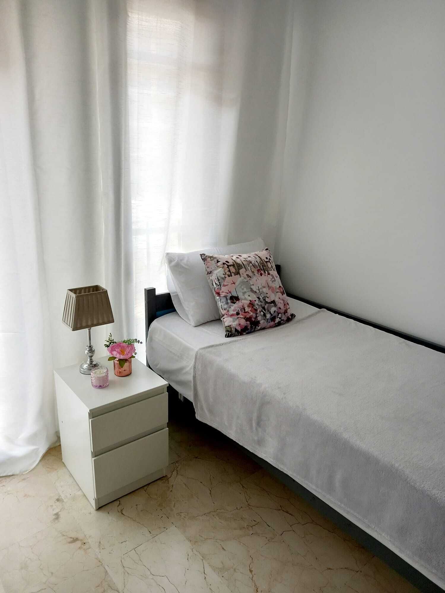 Una camera da letto con un letto singolo, un comodino con una lampada e un tavolino con un vaso e una candela.