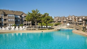 A swimming pool with lounge chairs, a wooden bridge, and a building with multiple balconies.