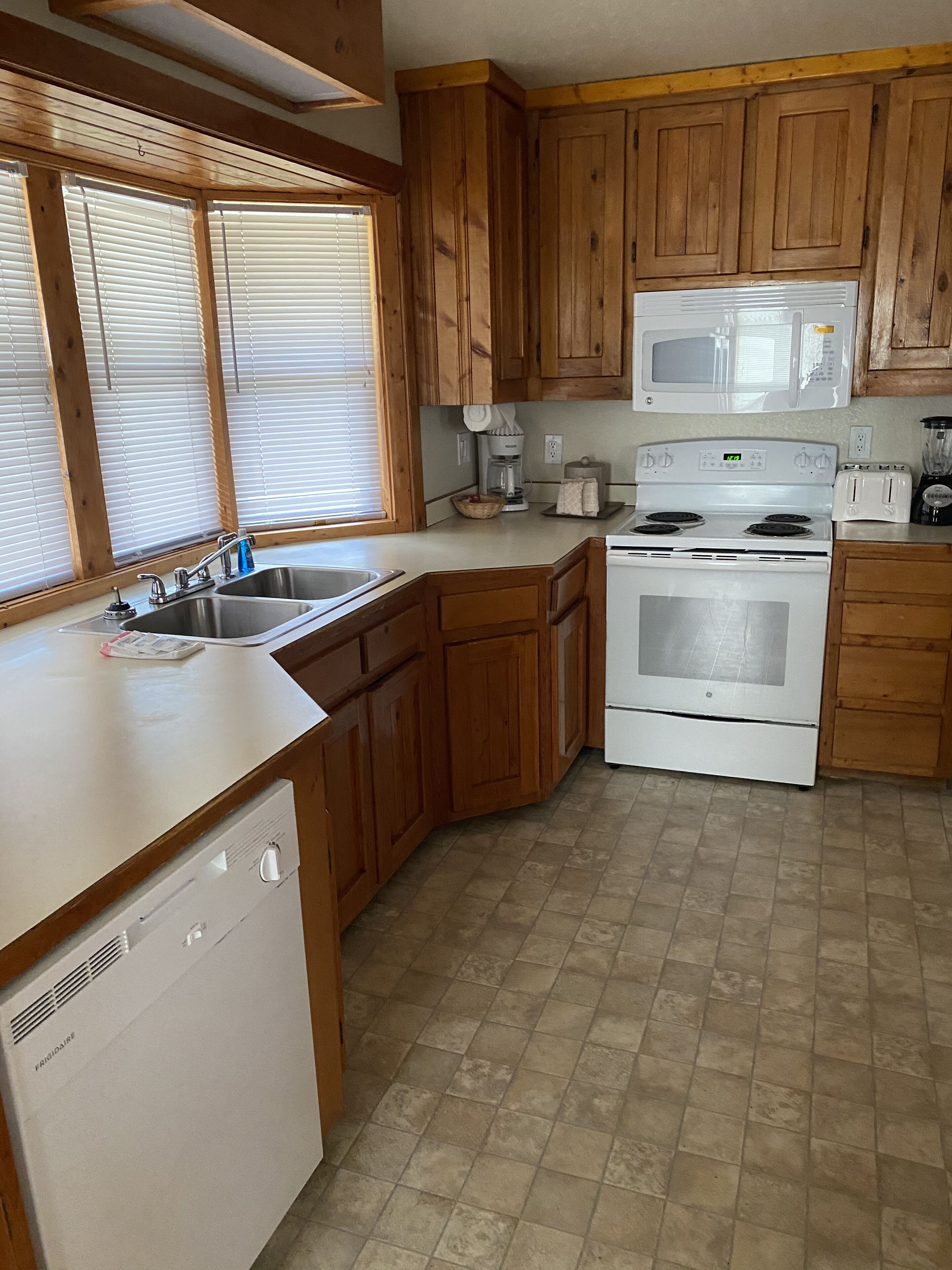 A kitchen with wooden cabinets, a white dishwasher, a stove, a microwave, and a coffee maker.