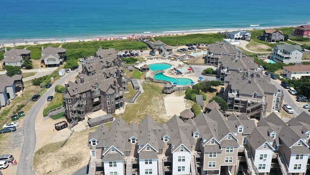A coastal residential area with multiple houses, a swimming pool, and a beach in the background.