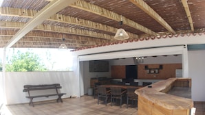 An outdoor patio with a wooden bench, a dining table with chairs, a kitchen area, and a wooden counter.