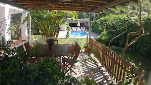 A covered patio with a pool, wooden deck, and outdoor furniture.