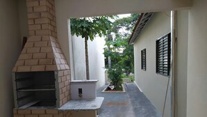 A narrow outdoor corridor with a brick-built barbecue grill and a small planter with a tree.