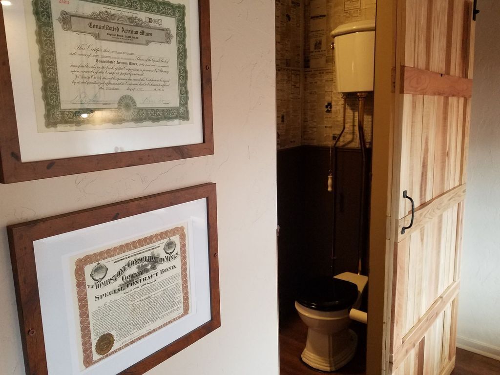 Gerahmte Zertifikate an einer Wand, eine Holztür und eine Toilette in einem Raum.