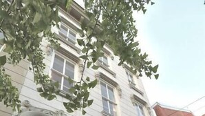 Een meerlaags gebouw met een witte gevel, grote ramen en een balkon met zwarte leuningen.