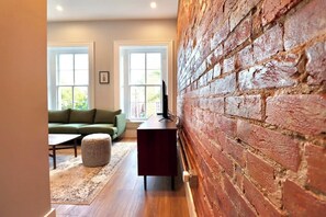 A room with a brick wall, a green sofa, a small ottoman, and a wooden coffee table. - The Franklin Suite at Prince Street Inn (Alexandria)