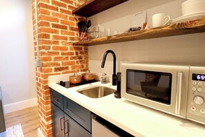 Une cuisine avec un mur en briques, un évier en acier inoxydable, un four à micro-ondes et des étagères en bois au-dessus du plan de travail.