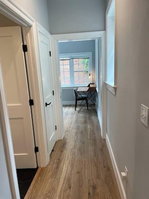 A hallway with a wooden floor, white doors, and a window with a view of greenery. - The King Suite at Prince Street Inn, ADA Accessible (Alexandria)