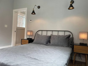 A bedroom with a bed, two bedside lamps, a nightstand, and a window with blinds. - The King Suite at Prince Street Inn, ADA Accessible (Alexandria)