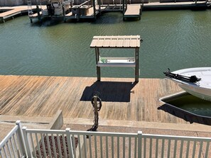 A wooden dock with a small shelter, a boat docked to the right, and a marina in the background.