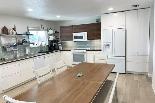 A modern kitchen with white cabinets, a wooden dining table, and a built-in oven. - Texas Grand Slam (City-by-the Sea)