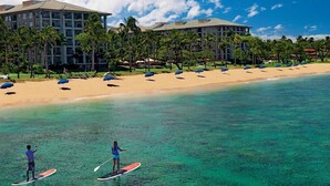 Ein Strandresort mit klarem türkisblauem Wasser, Paddleboardern und einem mehrstöckigen Hotel mit Palmen.