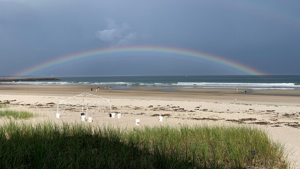 Ein Strand mit Regenbogen, einer weißen Struktur und einigen Personen.